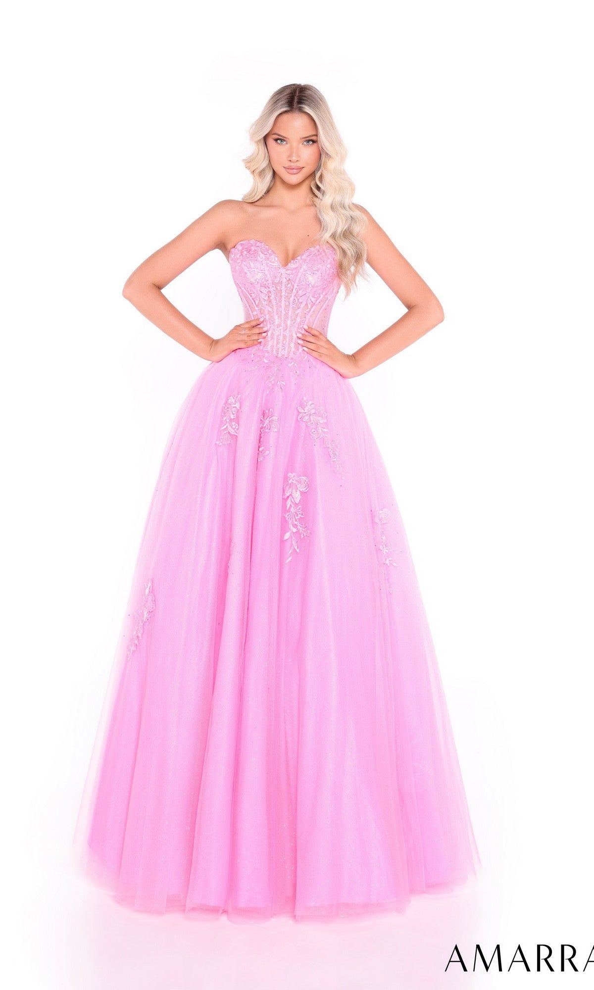A woman wears the Amarra 89011 Lace-Up Strapless Prom Ball Gown, a floor-length pink dress with a fitted sweetheart bodice and floral embellishments.